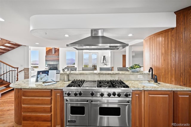 kitchen featuring light stone countertops, range with two ovens, light hardwood / wood-style floors, and wall chimney range hood