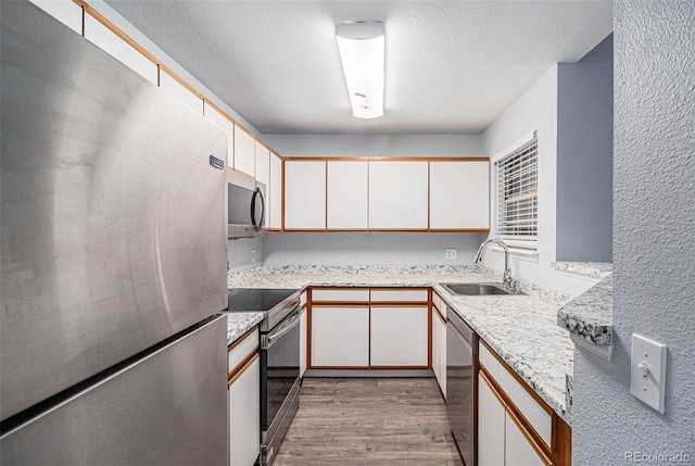 kitchen with sink, a textured ceiling, appliances with stainless steel finishes, light hardwood / wood-style floors, and white cabinetry