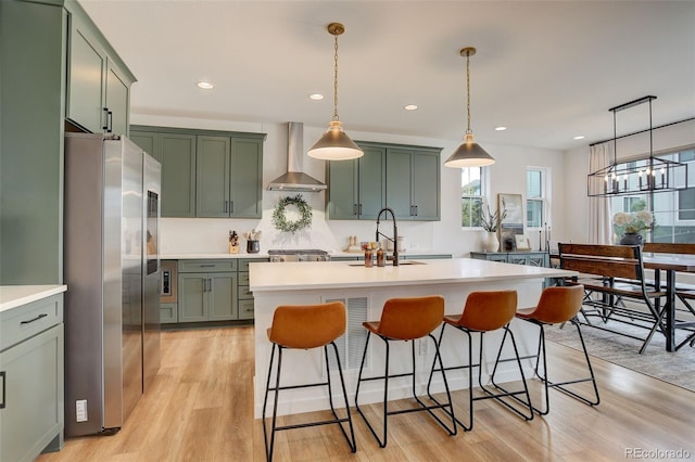 kitchen with light wood-type flooring, appliances with stainless steel finishes, sink, wall chimney range hood, and pendant lighting