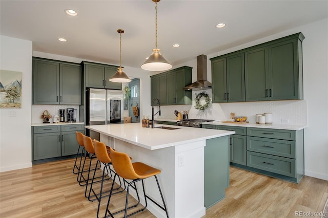 kitchen featuring an island with sink, light hardwood / wood-style flooring, sink, and wall chimney exhaust hood