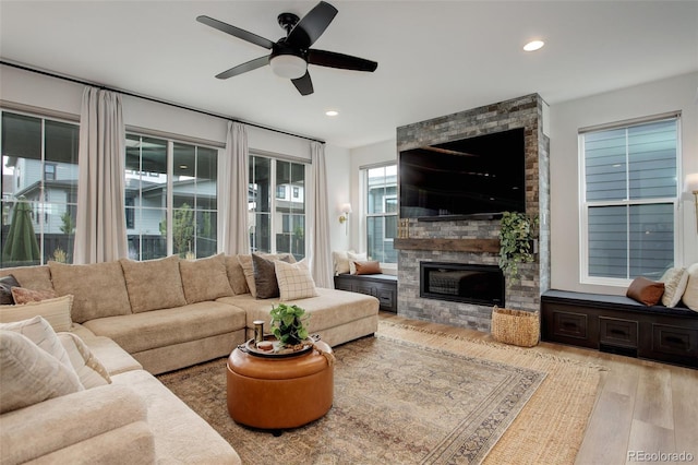 living room featuring light wood-type flooring, ceiling fan, and a stone fireplace