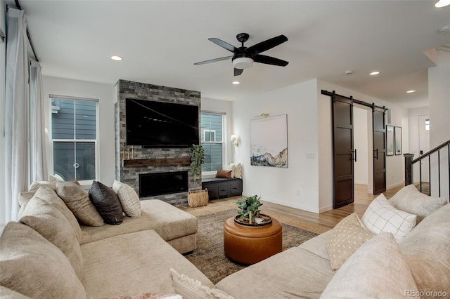 living room featuring light hardwood / wood-style floors, ceiling fan, a barn door, and a stone fireplace