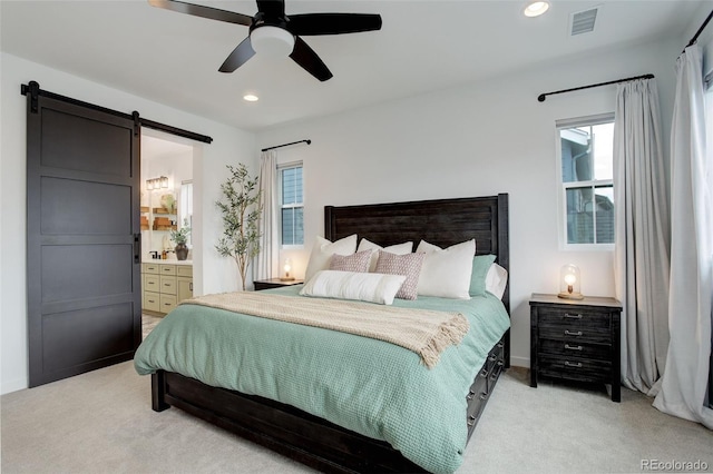 bedroom featuring a barn door, multiple windows, ceiling fan, and ensuite bath