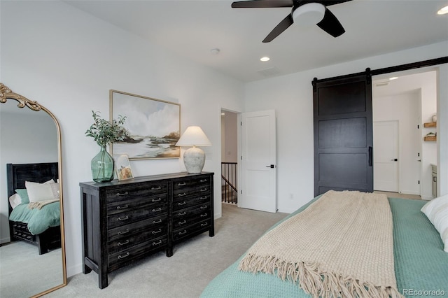 bedroom with light colored carpet, ceiling fan, and a barn door