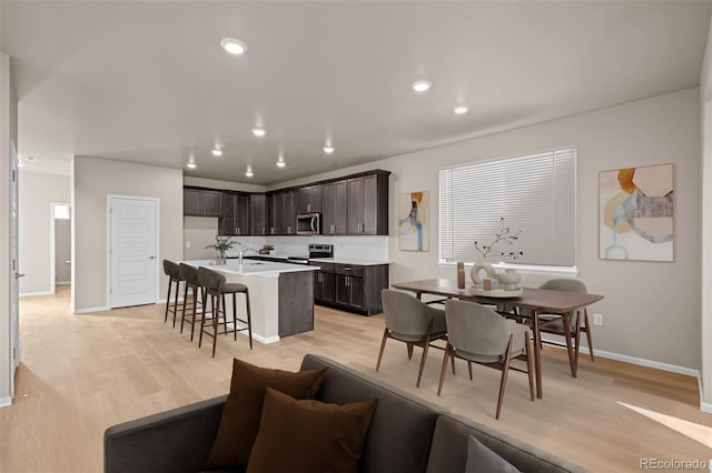 kitchen featuring a kitchen bar, dark brown cabinets, light hardwood / wood-style flooring, appliances with stainless steel finishes, and an island with sink