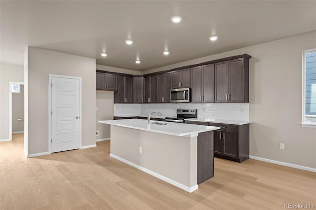 kitchen with appliances with stainless steel finishes, sink, a kitchen island with sink, light hardwood / wood-style floors, and dark brown cabinets