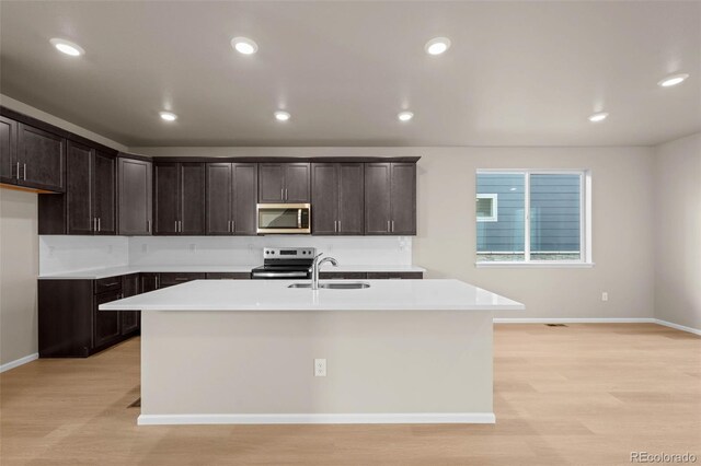 kitchen with sink, light hardwood / wood-style flooring, a kitchen island with sink, dark brown cabinets, and stainless steel appliances