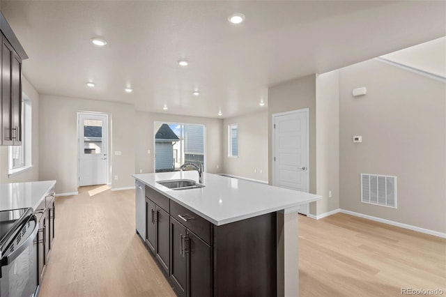 kitchen featuring black electric range oven, sink, dark brown cabinetry, light hardwood / wood-style floors, and an island with sink