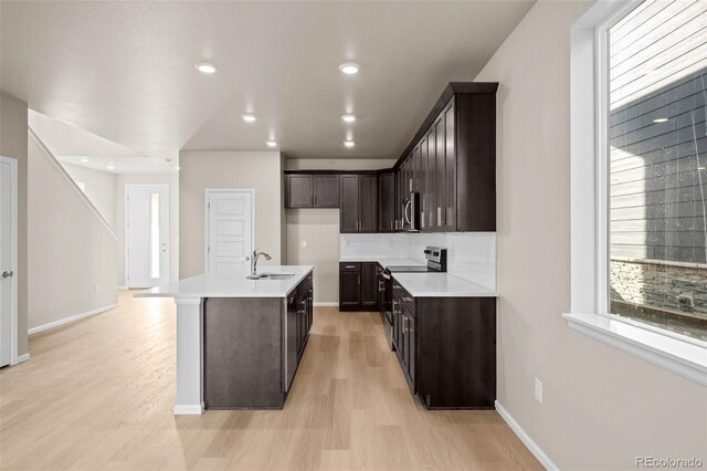 kitchen featuring sink, appliances with stainless steel finishes, dark brown cabinetry, light hardwood / wood-style floors, and a center island with sink