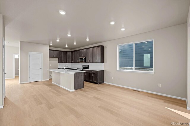 kitchen featuring dark brown cabinetry, sink, appliances with stainless steel finishes, a kitchen island with sink, and light hardwood / wood-style floors