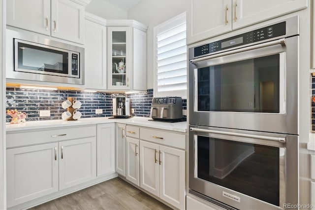 547 Scrubjay Cir, Castle Rock, CO 80104 - kitchen with appliances with stainless steel finishes, white cabinetry, light countertops, glass insert cabinets, and decorative backsplash