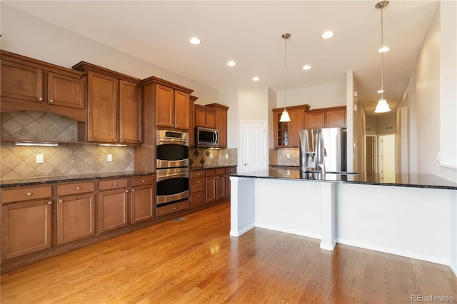 kitchen with decorative light fixtures, dark stone countertops, appliances with stainless steel finishes, light wood-style floors, and brown cabinetry