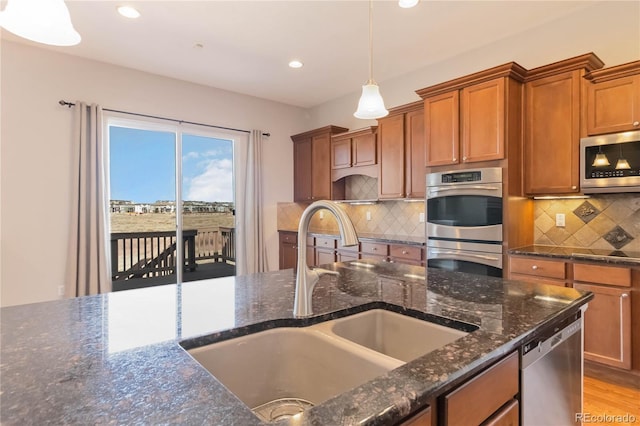 kitchen featuring a sink, decorative light fixtures, dark stone counters, appliances with stainless steel finishes, and brown cabinetry