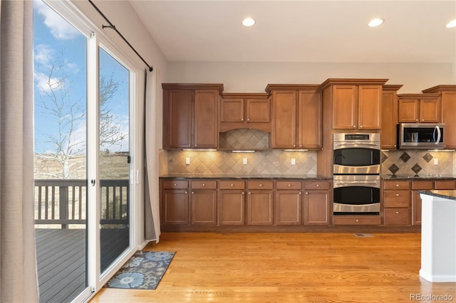 kitchen with dark countertops, light wood finished floors, tasteful backsplash, brown cabinets, and stainless steel appliances