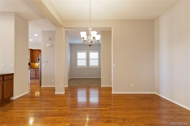 empty room with a chandelier, recessed lighting, light wood-style flooring, and baseboards