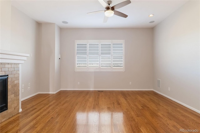 unfurnished living room featuring a brick fireplace, baseboards, light wood-type flooring, and a ceiling fan