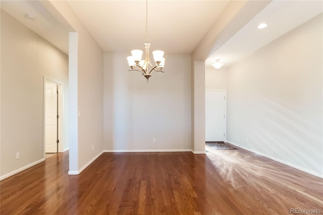 spare room with baseboards, an inviting chandelier, and dark wood finished floors