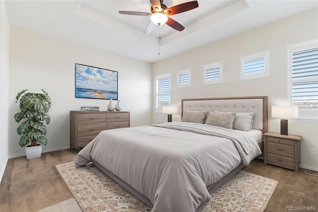 bedroom with baseboards, carpet, a tray ceiling, and a ceiling fan