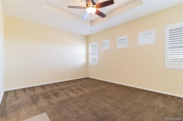 empty room featuring a ceiling fan, a raised ceiling, baseboards, and dark colored carpet