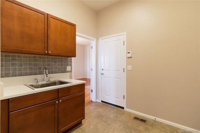 kitchen with baseboards, visible vents, a sink, decorative backsplash, and light countertops