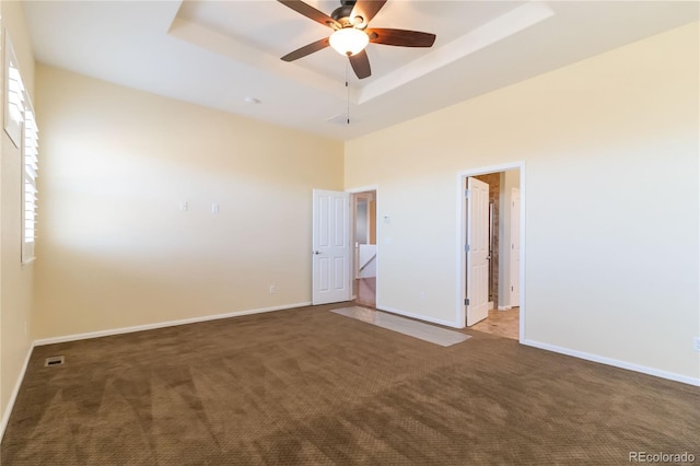 empty room featuring a raised ceiling, carpet flooring, a ceiling fan, and baseboards