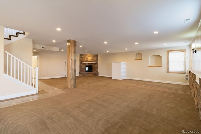 unfurnished living room featuring a stone fireplace, recessed lighting, stairs, and carpet