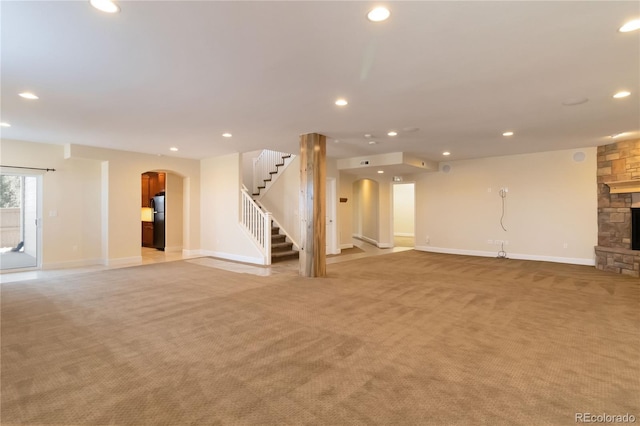 unfurnished living room featuring light carpet, recessed lighting, arched walkways, a stone fireplace, and stairs