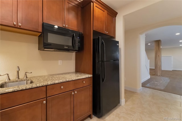 kitchen featuring light stone counters, brown cabinetry, arched walkways, a sink, and black appliances