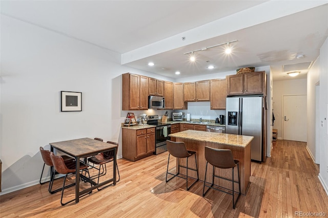 kitchen featuring a kitchen island, appliances with stainless steel finishes, a kitchen breakfast bar, light stone countertops, and light wood-type flooring