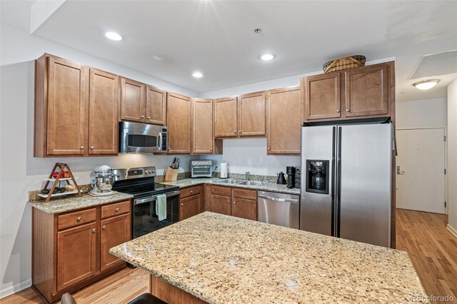 kitchen with light stone counters, stainless steel appliances, sink, and light wood-type flooring