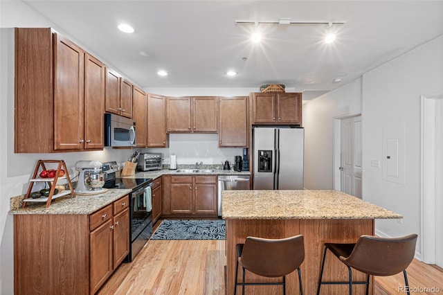 kitchen featuring track lighting, sink, light wood-type flooring, stainless steel appliances, and a breakfast bar