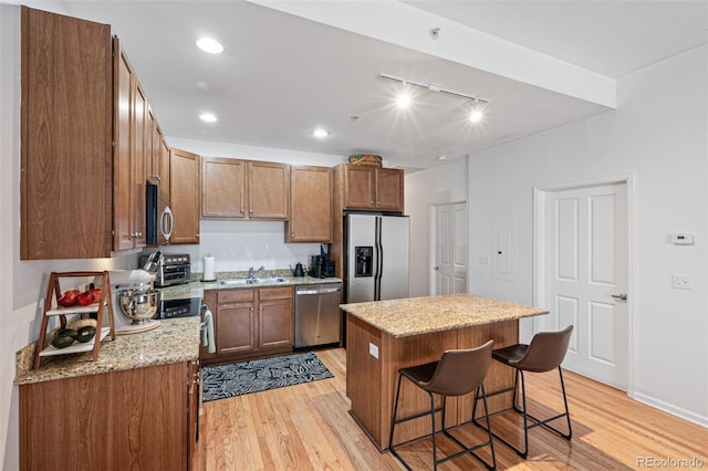 kitchen featuring light hardwood / wood-style flooring, stainless steel appliances, sink, a center island, and a kitchen bar