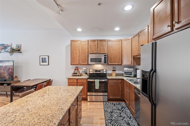 kitchen featuring stainless steel appliances, light stone countertops, light hardwood / wood-style flooring, and track lighting