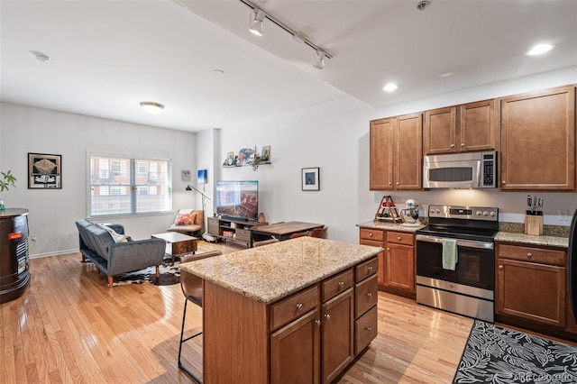 kitchen featuring appliances with stainless steel finishes, a kitchen bar, a kitchen island, light hardwood / wood-style floors, and track lighting