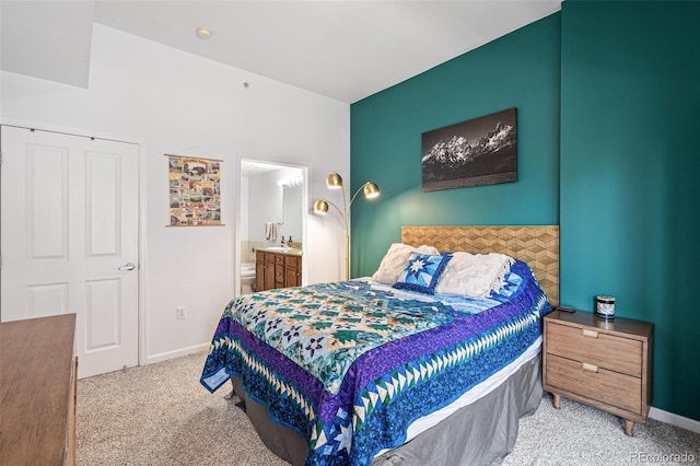 bedroom with ensuite bathroom and light colored carpet