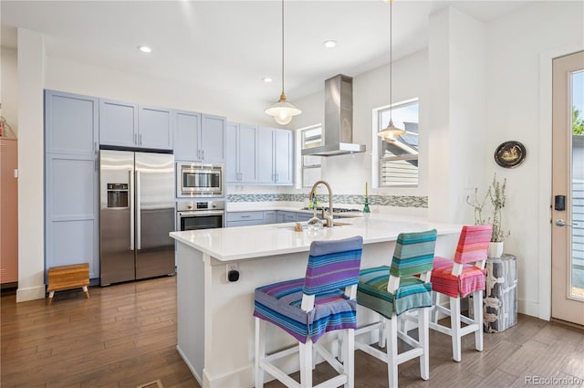 4958 Valentia Ct, Denver, CO 80238 - kitchen featuring appliances with stainless steel finishes, wall chimney range hood, a peninsula, a kitchen breakfast bar, and light countertops