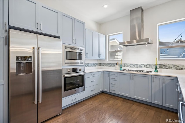 4958 Valentia Ct, Denver, CO 80238 - kitchen with stainless steel appliances, wall chimney exhaust hood, dark wood-type flooring, tasteful backsplash, and light countertops