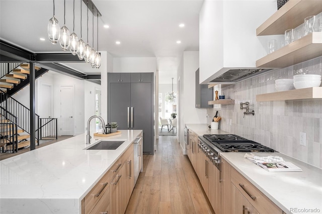 kitchen featuring sink, light hardwood / wood-style floors, tasteful backsplash, hanging light fixtures, and a center island with sink