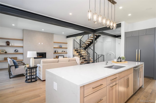 kitchen with decorative light fixtures, light brown cabinetry, sink, a center island with sink, and light hardwood / wood-style floors