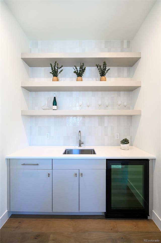 bar featuring backsplash, dark wood-type flooring, sink, and beverage cooler