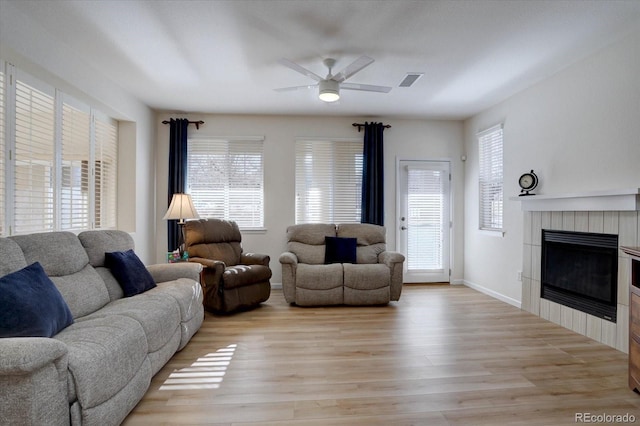 living room featuring visible vents, light wood-style flooring, ceiling fan, a tile fireplace, and baseboards