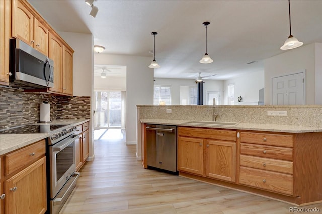 kitchen featuring tasteful backsplash, appliances with stainless steel finishes, decorative light fixtures, light wood-style floors, and a sink