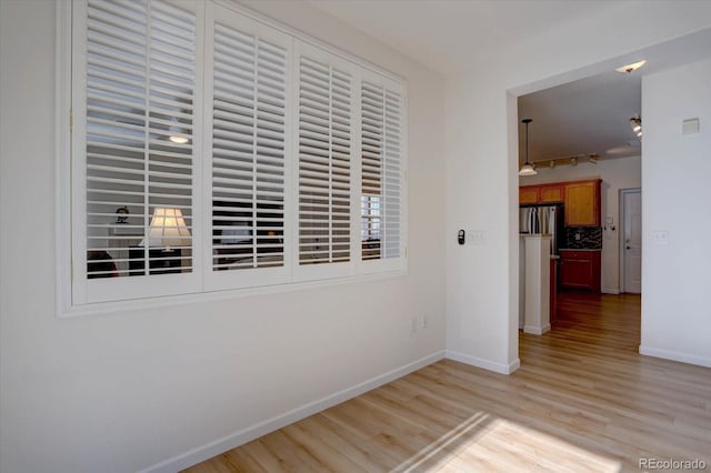 hallway with rail lighting, light wood-style flooring, and baseboards