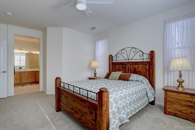 bedroom featuring ensuite bathroom, light colored carpet, a ceiling fan, baseboards, and visible vents