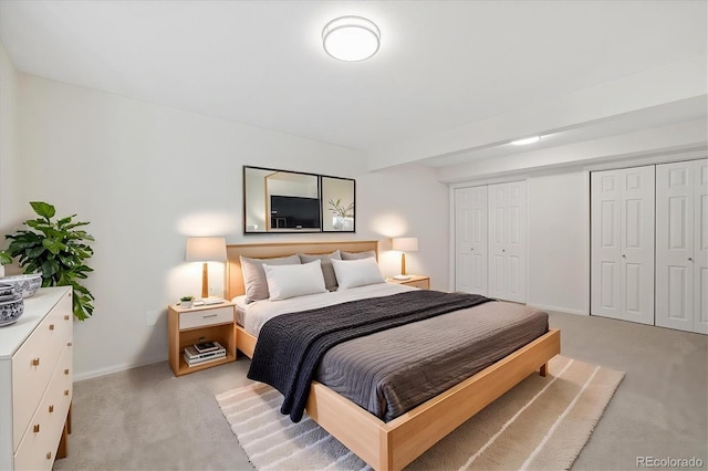 bedroom featuring light carpet, multiple closets, and baseboards