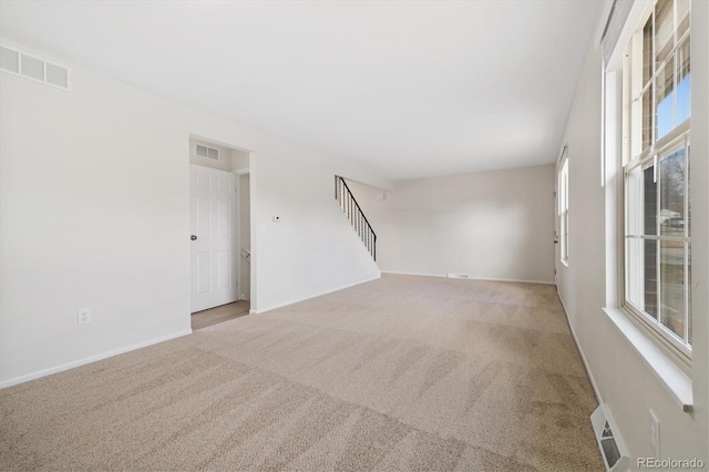 carpeted empty room featuring a healthy amount of sunlight, visible vents, and stairs