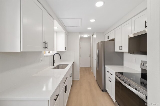 kitchen with light wood finished floors, stainless steel appliances, light countertops, white cabinetry, and a sink