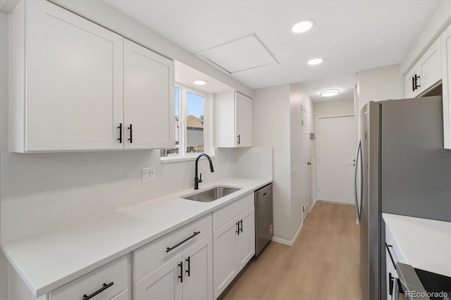 kitchen featuring light wood finished floors, stainless steel appliances, light countertops, white cabinets, and a sink