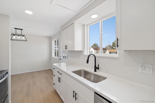 kitchen with light wood-type flooring, white cabinetry, light countertops, and a sink