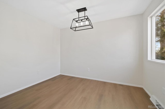 empty room featuring an inviting chandelier, wood finished floors, visible vents, and baseboards